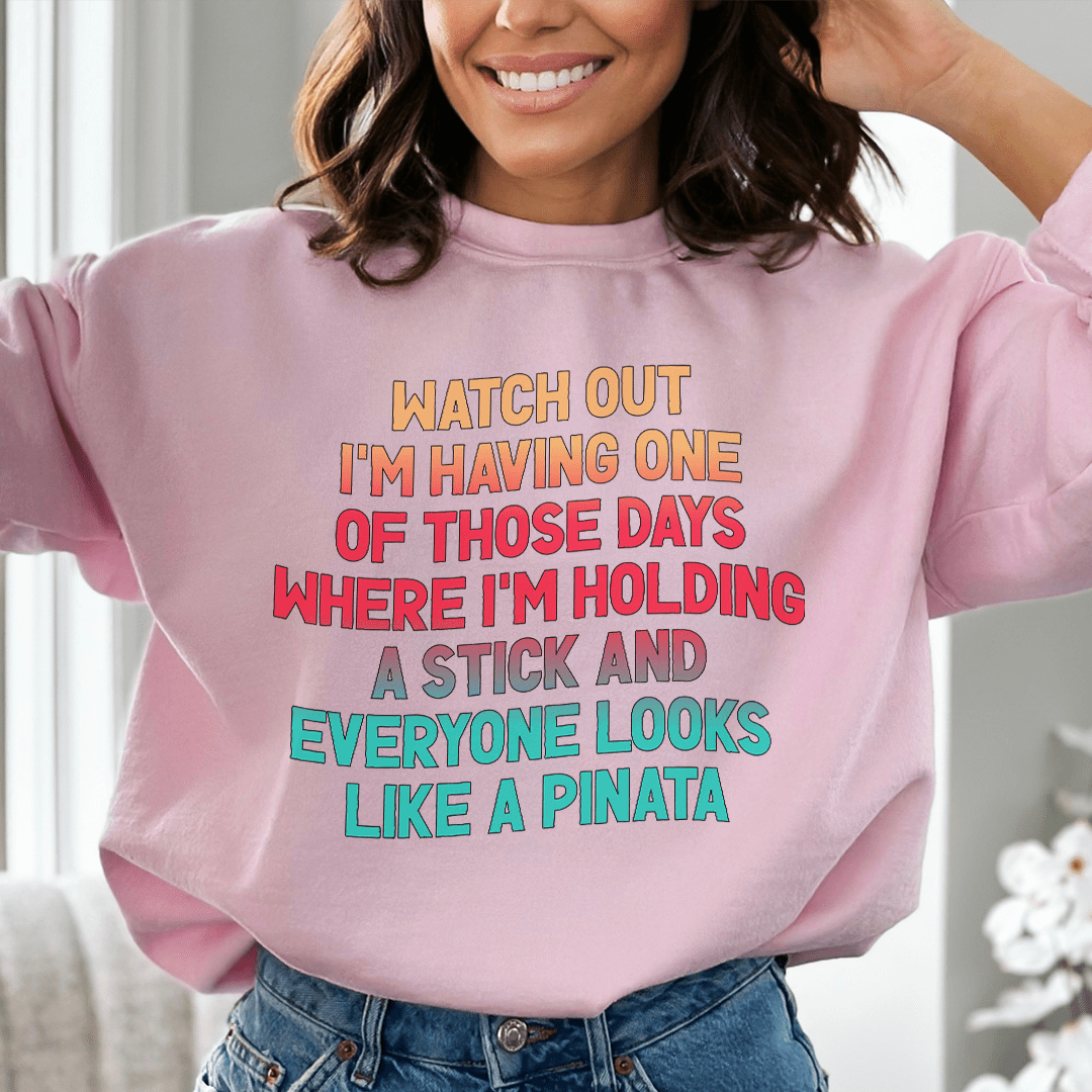 Merchmallow pink funny graphic sweatshirt with colorful text joke about holding a stick and pinatas worn by smiling woman