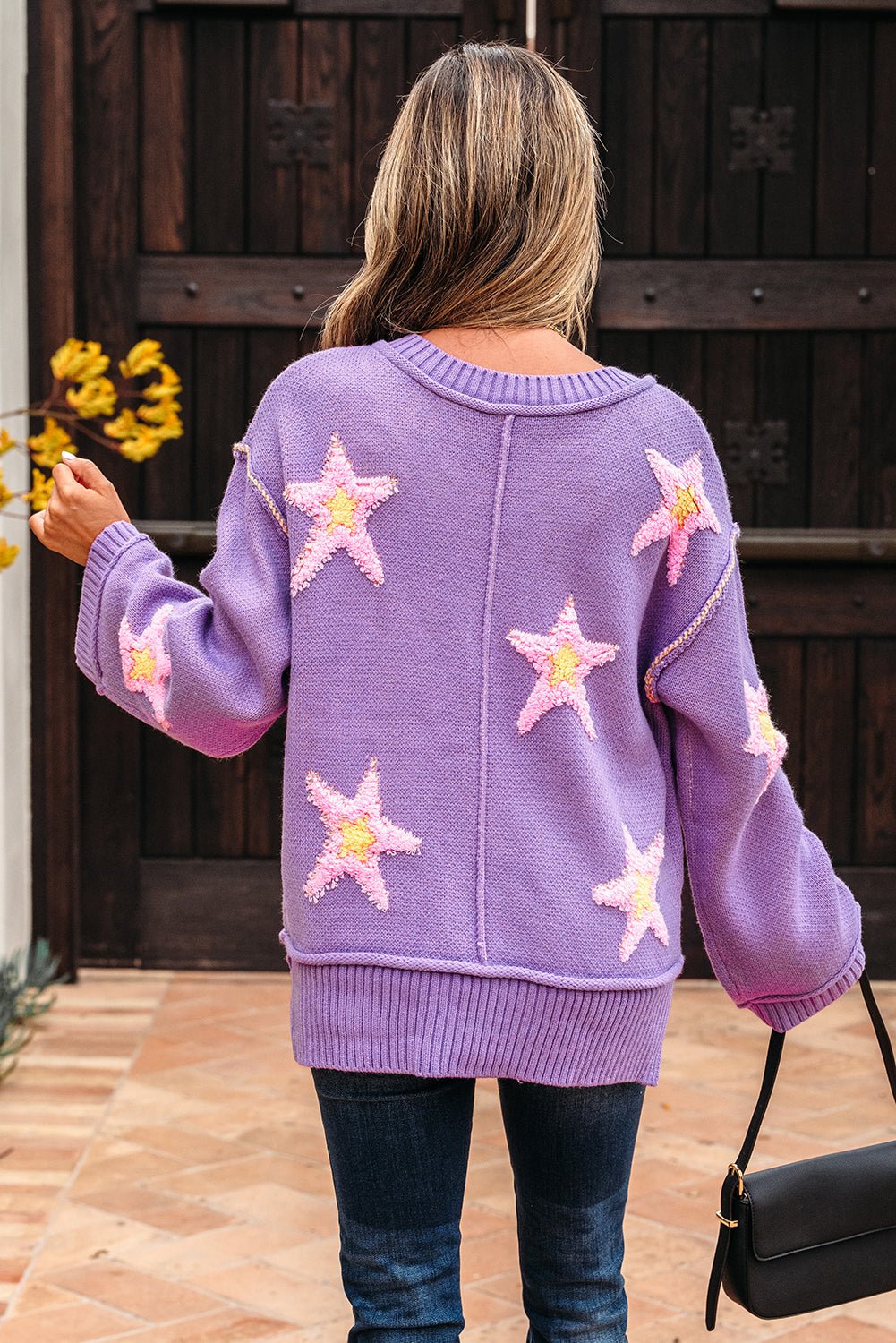 Back view of woman wearing Threaded Pear brushed star oversized sweater in lavender with pink stars and jeans